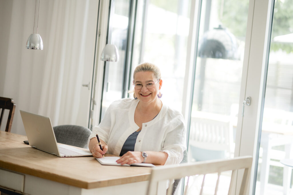 Anja Kruse mit Laptop und Notizbuch am Tisch sitzend