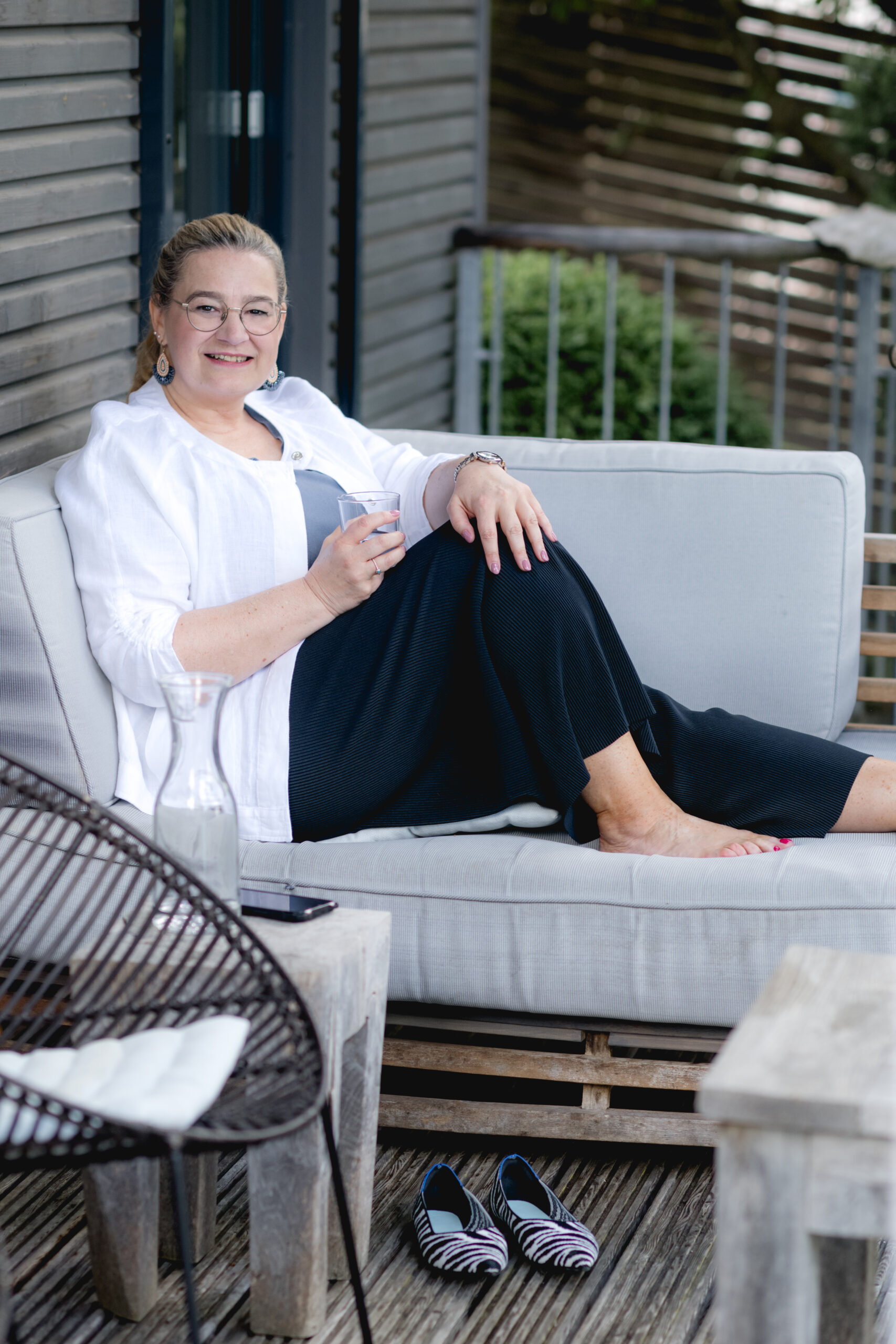 Anja Kruse auf einem Sofa sitzend mit Wasserglas in der Hand, outdoor