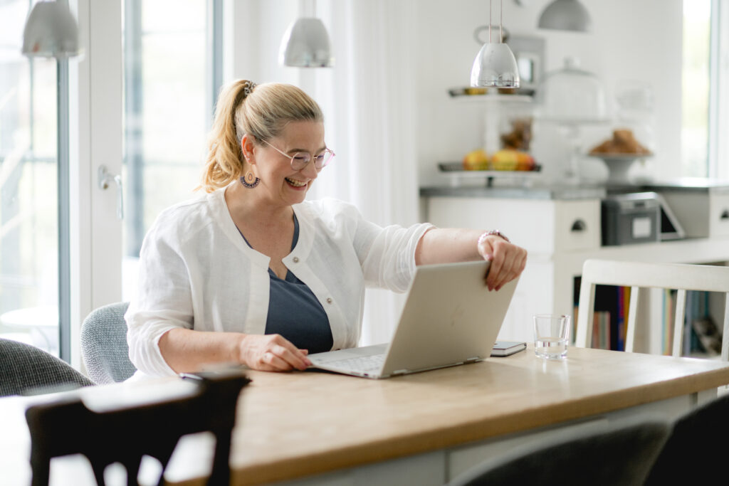 Anja Kruse mit Laptop froehlich am Tisch sitzend